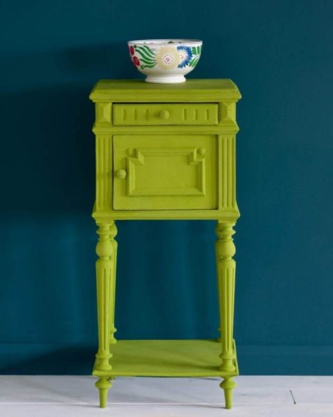 A bright green painted side table with a dark blue background. There is a small bowl on top.