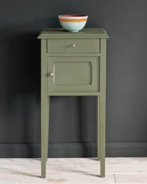 A painted side table in a dusky green chalk paint with a white and orange bowl on top