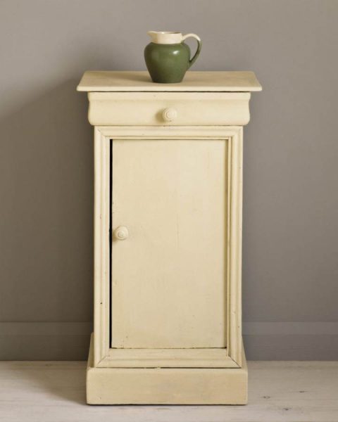 A painted side table in cream chalk paint. There is a green pottery jug on top.