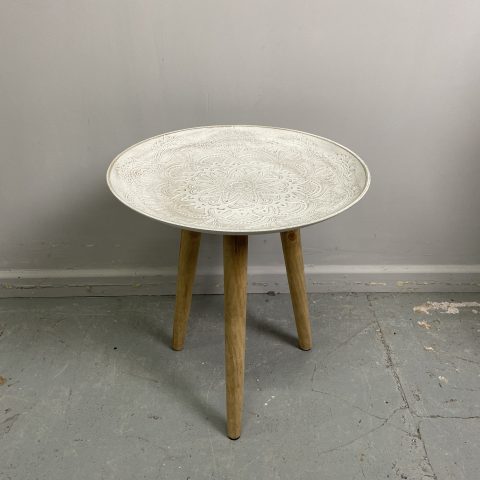 A round side table on a tripod base. The top is white with a floral textured pattern and the base is timber.