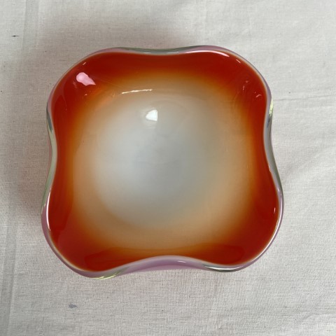 A squared shaped milk glass bowl with orange colouring inside