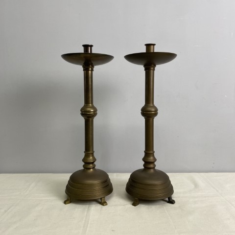 A pair of tall brass candlesticks with wide footed base and wax catcher at the top.