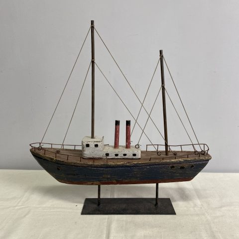 A decorative rustic sailing boat with two masts without sails made from reclaimed wood. It is displayed on a metal stand.