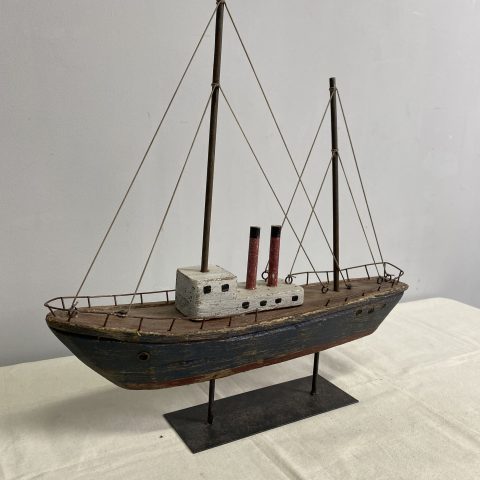 A decorative rustic sailing boat with two masts without sails made from reclaimed wood. It is displayed on a metal stand.