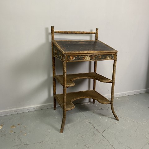 An antique standing height desk with tilted, lift-up desk top. It is constructed with bamboo and has painted details on the panels. It has 2 shelfs below the desktop with an arched cut out space.