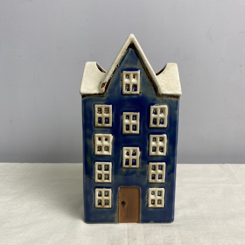 A tall ceramic vase or planter in the shape of a dark blue house with white roof