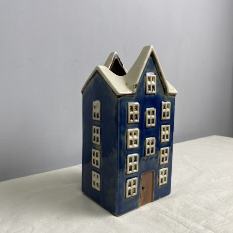 A tall ceramic vase or planter in the shape of a dark blue house with white roof