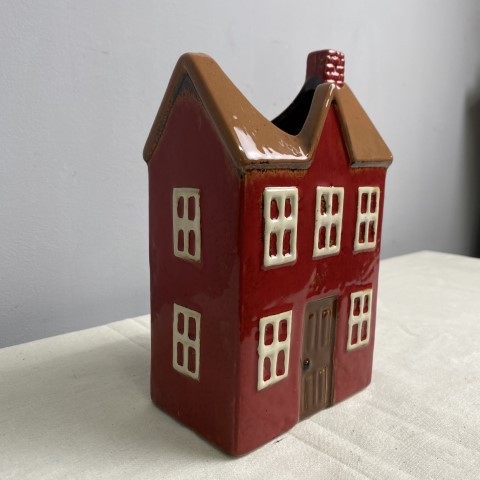 A ceramic vase or planter in the shape of a red house with a brown roof