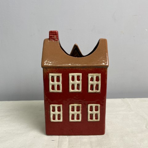 A ceramic vase or planter in the shape of a red house with a brown roof