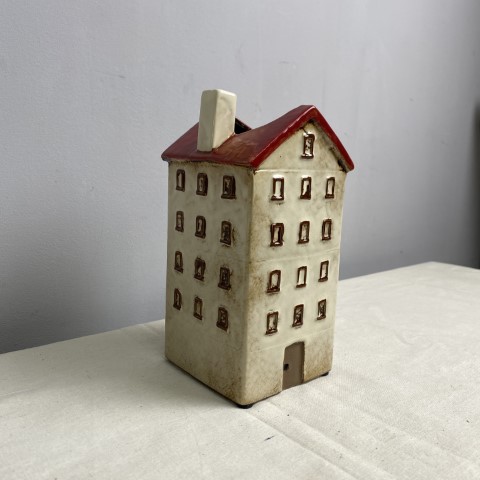 A tall ceramic vase or planter in the shape of a white house with a red roof