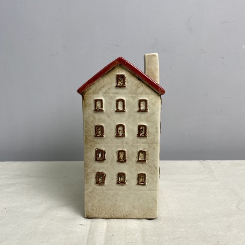 A tall ceramic vase or planter in the shape of a white house with a red roof