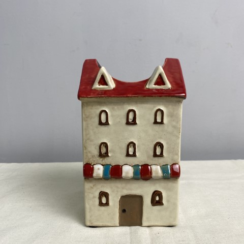A ceramic vase or planter in the shape of a white house with a red roof and red white and blue awning