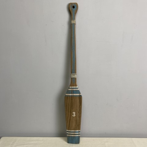 A rustic timber oar with white and aqua stripes