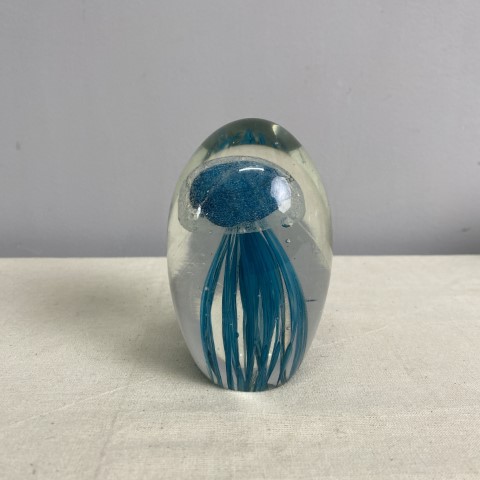A tall glass paperweight encasing a teal jellyfish