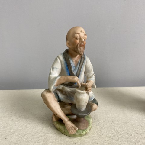 A bisque figure of a man sitting making a pot