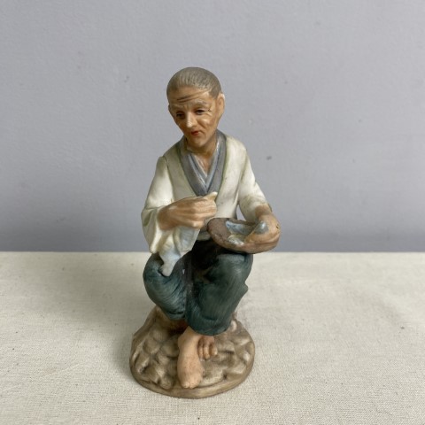 A bisque figure of a man sitting crafting a bowl