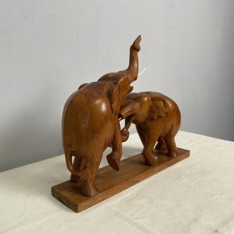 A timber statue of two elephants engaged in a play fight