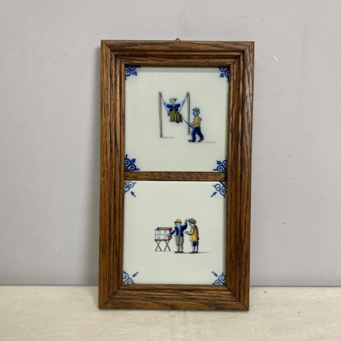A set of 2 Dutch tiles mounted in a wooden frame. The tiles depict children playing