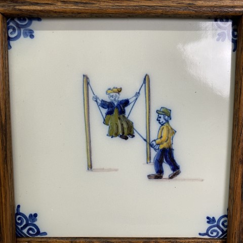 A set of 2 Dutch tiles mounted in a wooden frame. The tiles depict children playing