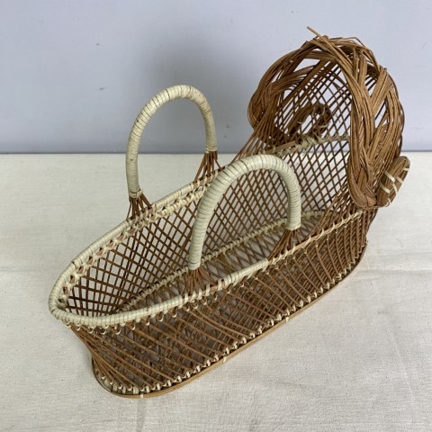 A vintage wicker wine carrier shaped like a doll bassinet with carry handles