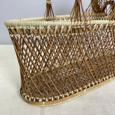 A vintage wicker wine carrier shaped like a doll bassinet with carry handles