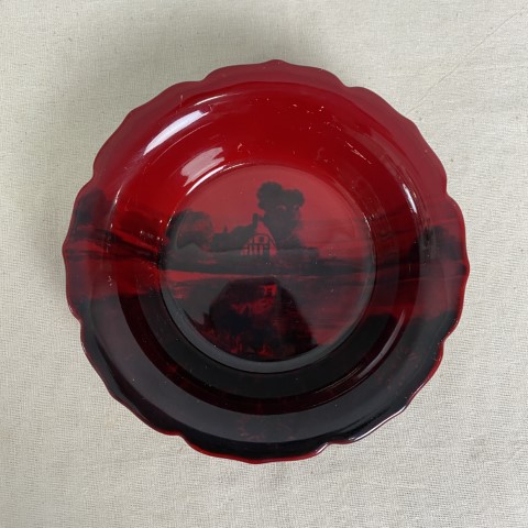 A red glass dish or ashtray with black image of a house and garden