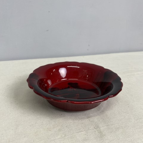 A red glass dish or ashtray with black image of a house and garden
