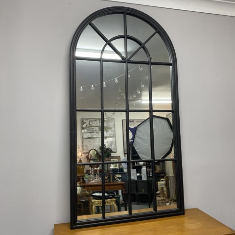 a tall black, arched mirror with window-like mouldings