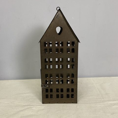 A rustic metal lantern in the shape of a house with many cut-out windows. It hangs on a chain.