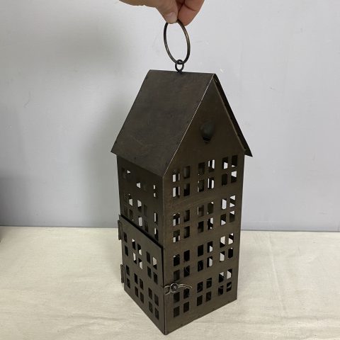 A rustic metal lantern in the shape of a house with many cut-out windows. It hangs on a chain.