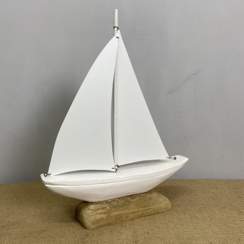 White model sailboat with white metal sails on driftwood stand